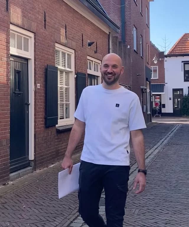 Coen Wilterdink loopt met een tekening onder de arm door een straat met oude woningen
